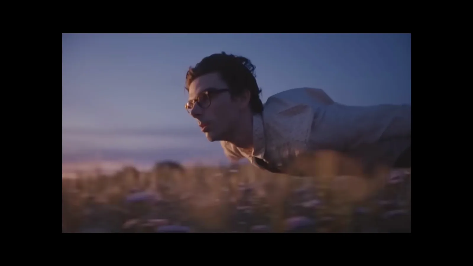 Sora 2 generated shot of a young man flying low over a dusk wheat field with his tie trailing behind him